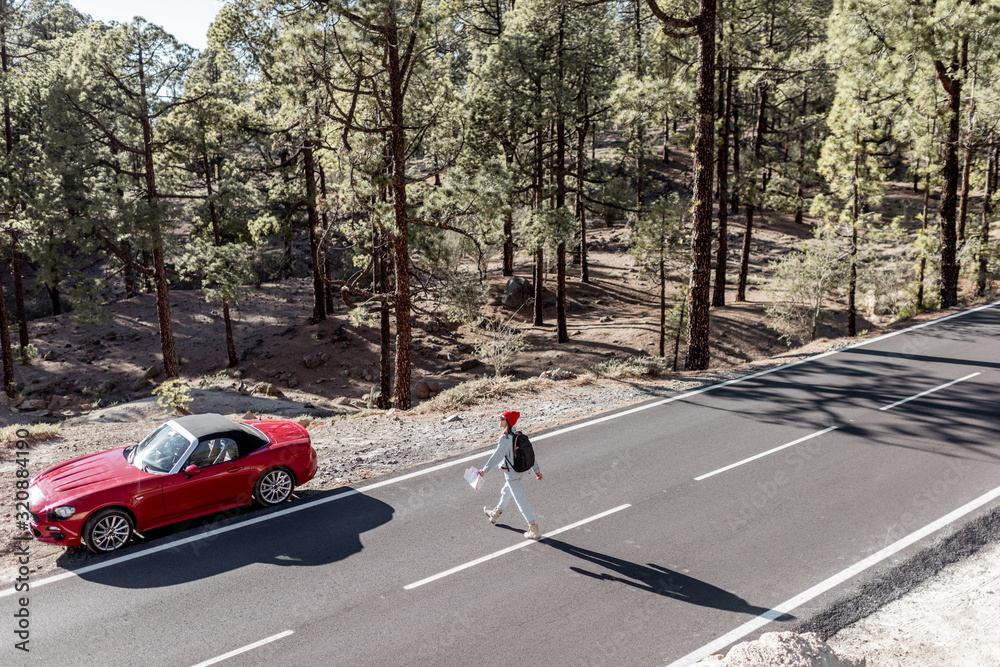 Carefree woman walking on the mountain road while traveling by car alone. Wide view from above with 