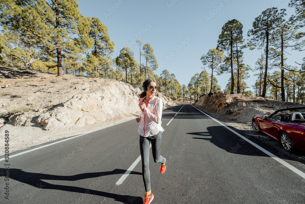 Young woman in sportswear jogging on the beautiful mountain road in the forest