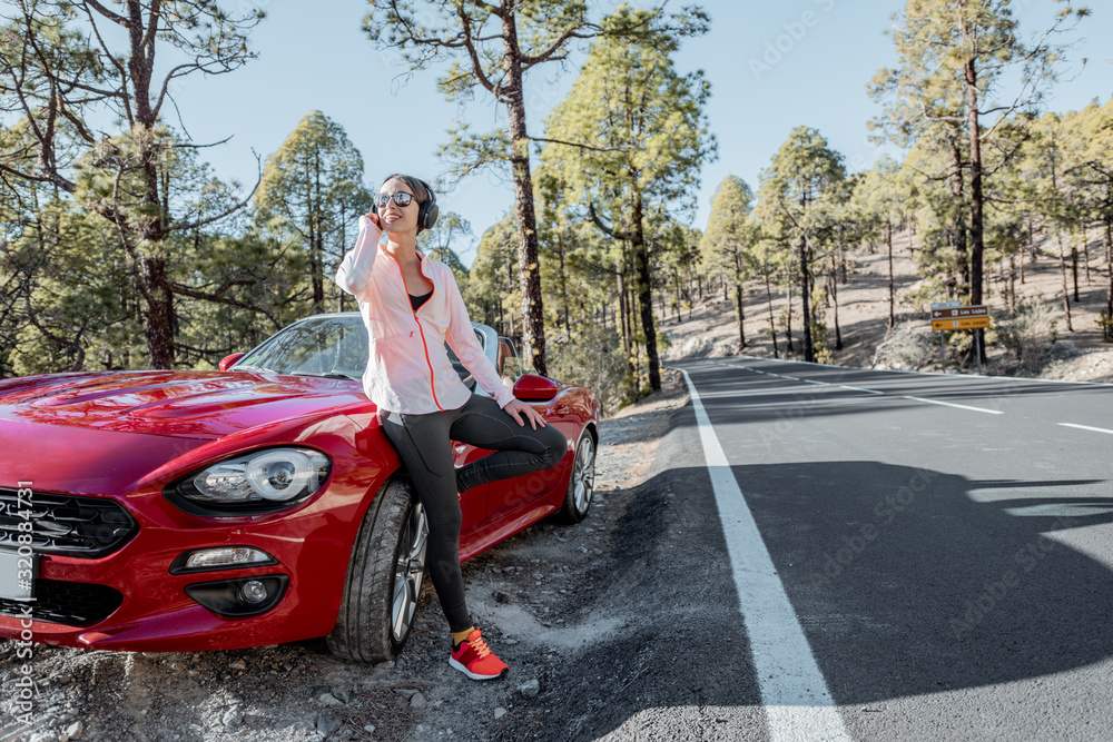 Young woman in sportswear standing near the car on the roadside, having a break after the training a