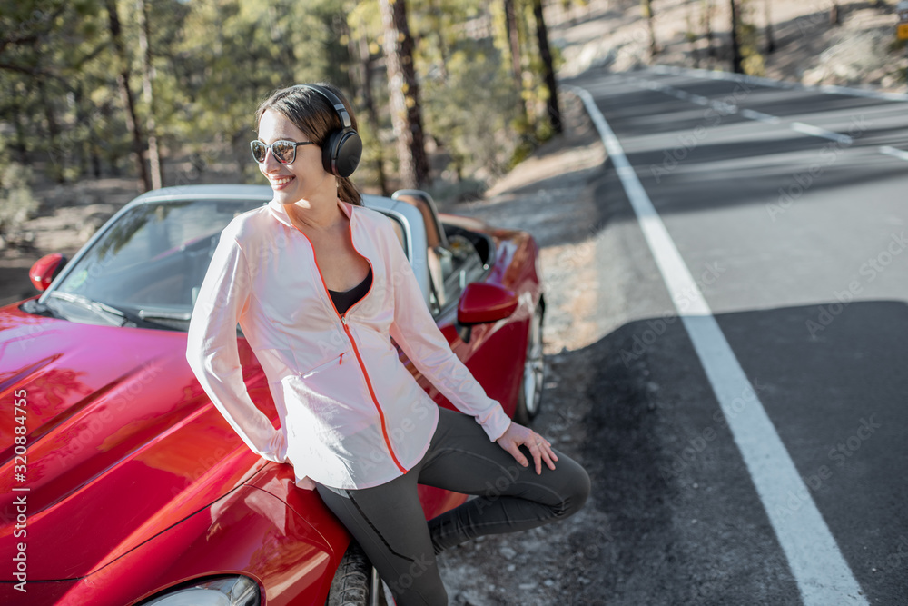 Young woman in sportswear standing near the car on the roadside, having a break after the training a