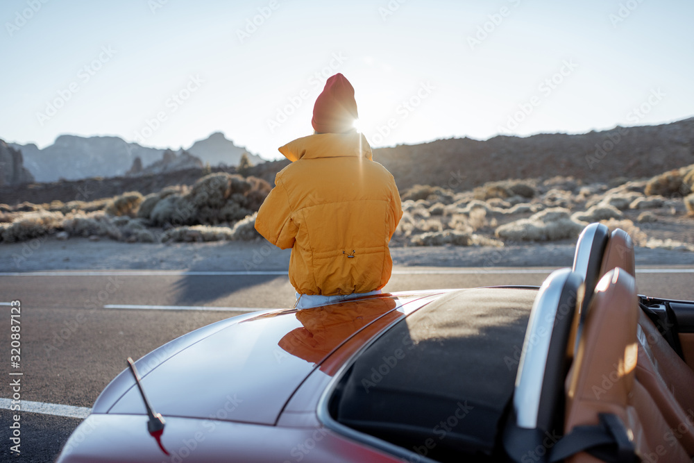 Woman enjoying beautiful volcanic landscapes, photographing on phone on the roadside during a sunset