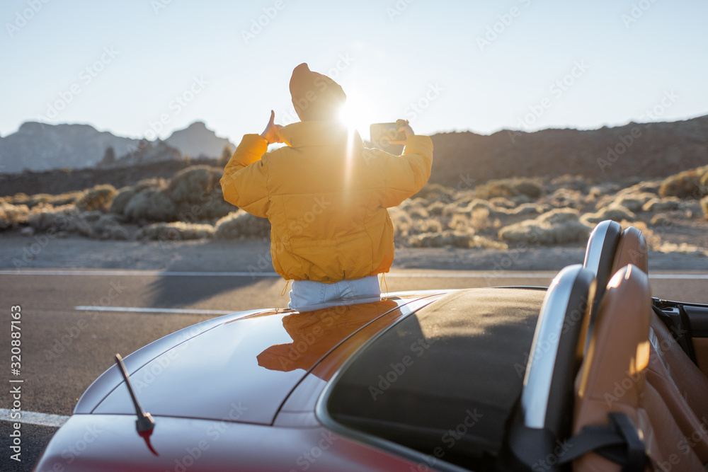 Woman enjoying beautiful volcanic landscapes, photographing on phone on the roadside during a sunset