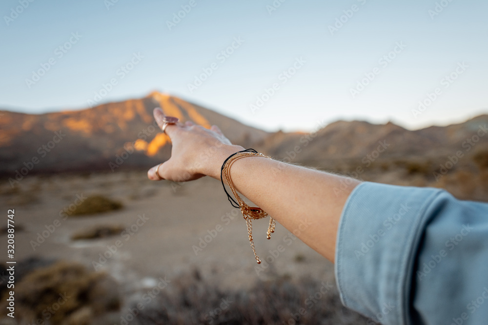 Woman pointing with hand on the volcanic mountain during a sunset, close-up on hand