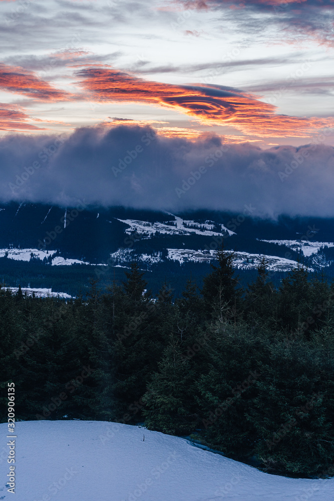 Dramatic sunset or sunrise with clouds in orange and blue colors. Mountain landscape. Rare lenticula