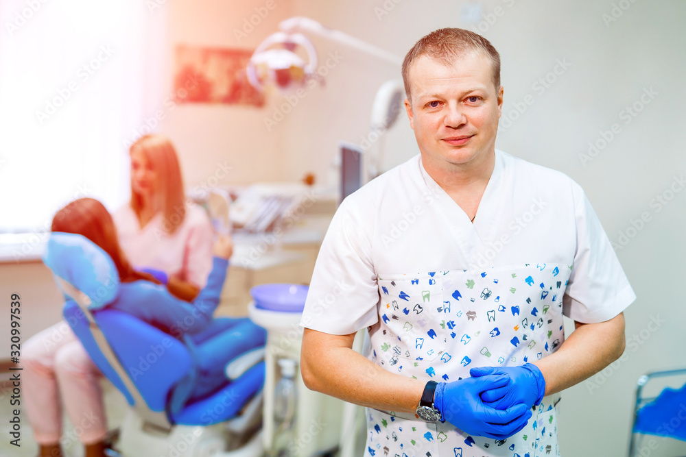 Doctor inviting you to dentist office and looking at camera with stomatological chair and patient in