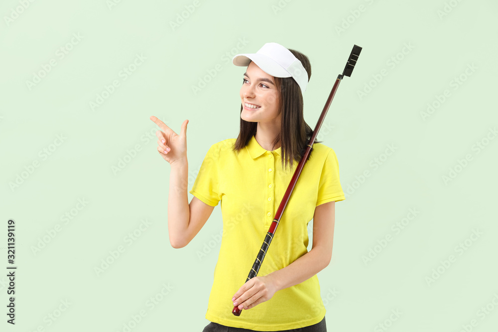 Beautiful female golfer pointing at something on color background