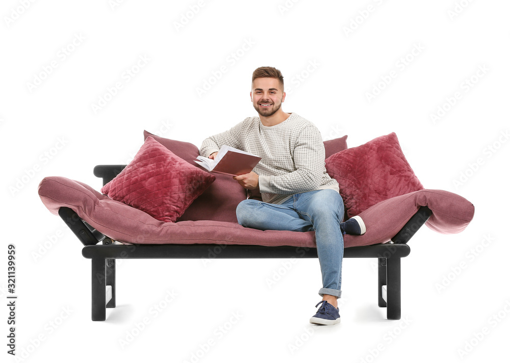 Young man reading book while sitting on sofa against white background