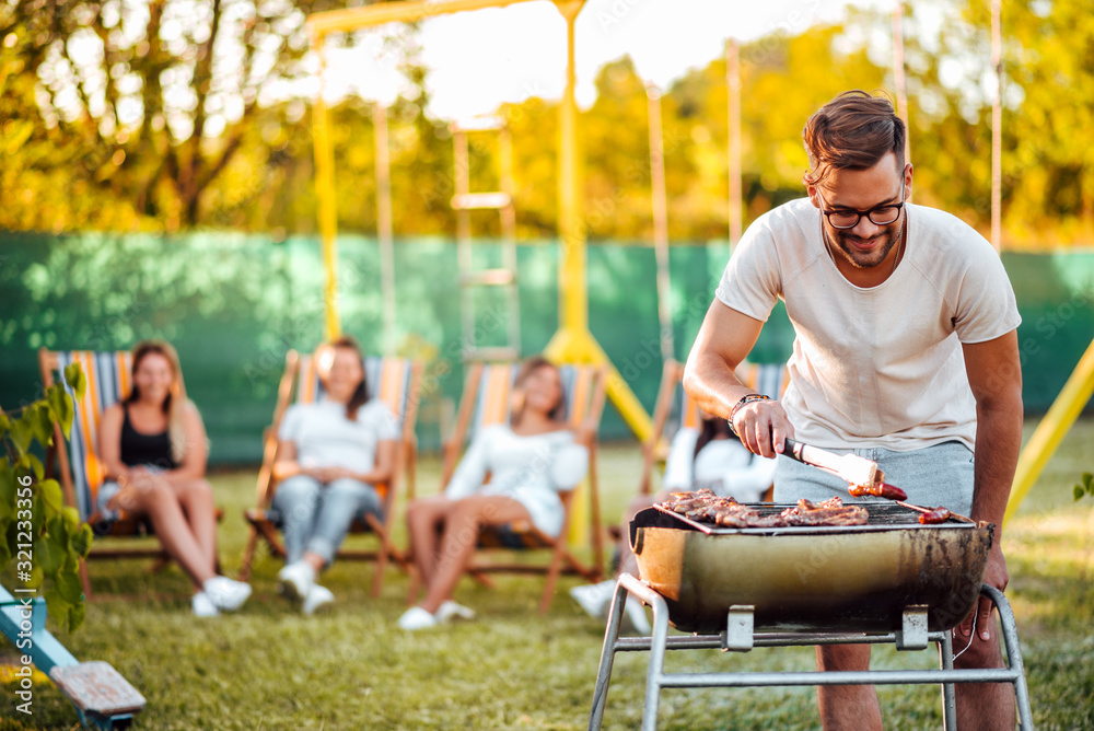 Friends having a barbecue party outdoors. Portrait of a handsome man cooking meat on a grill.