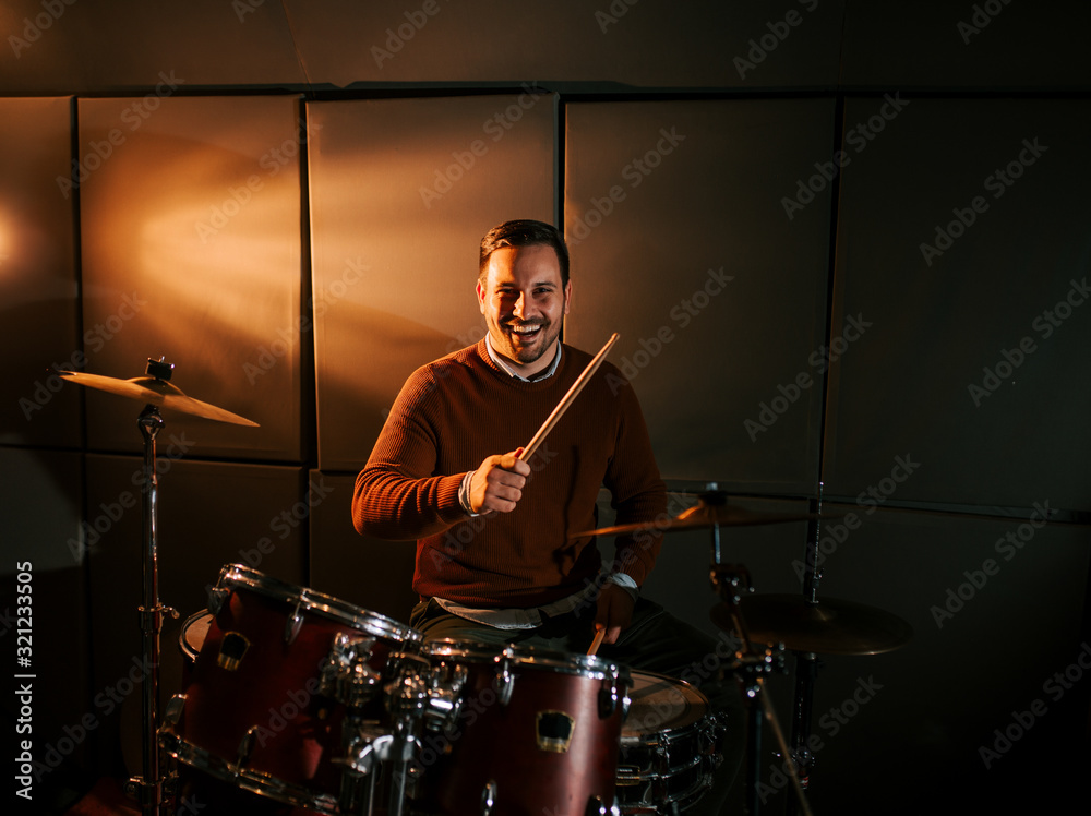 Portrait of a happy drummer playing drums and smiling at camera.