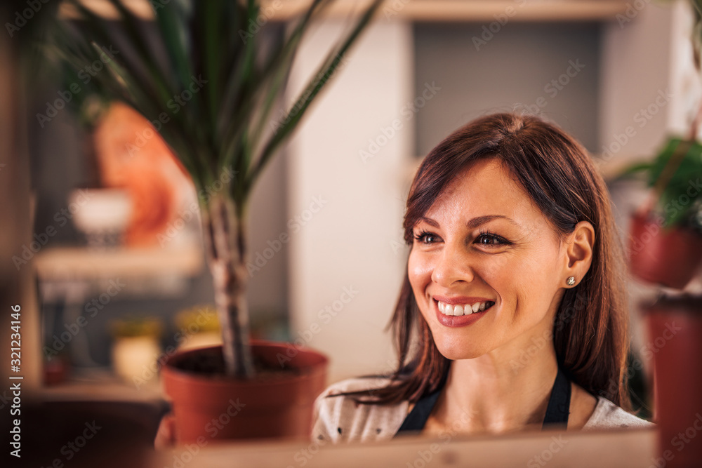 Head shot portrait of a happy woman holding flowerpot with house plant.