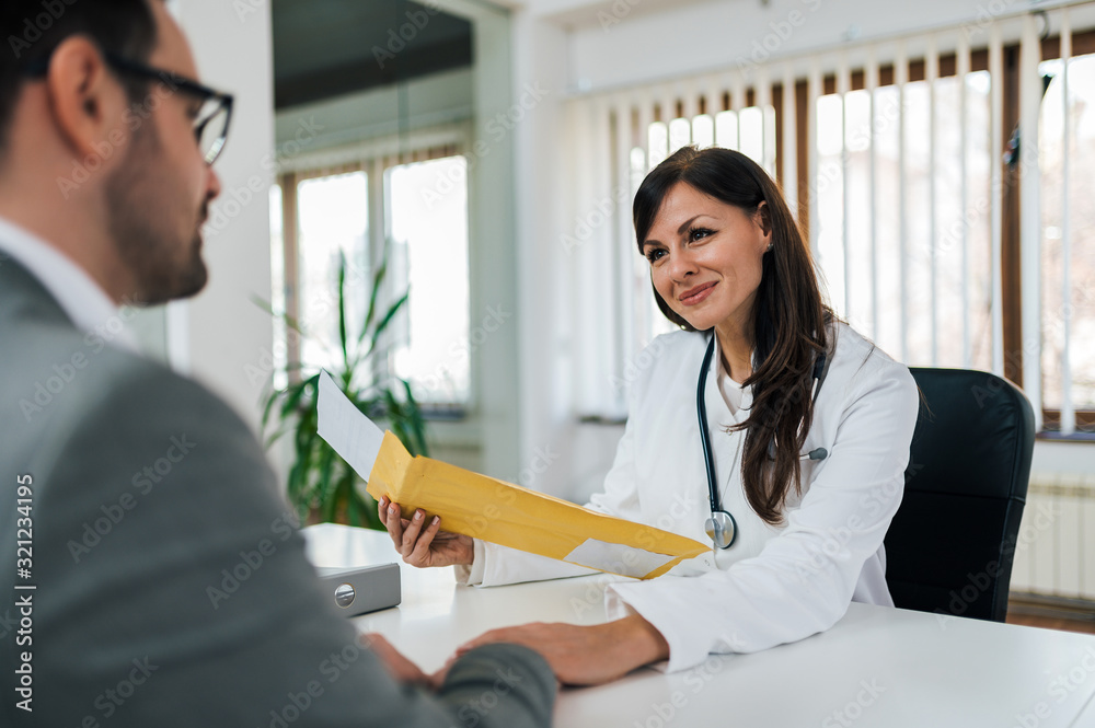 Portrait of a caring doctor at medical exam with a patient, holding envelope with test results.