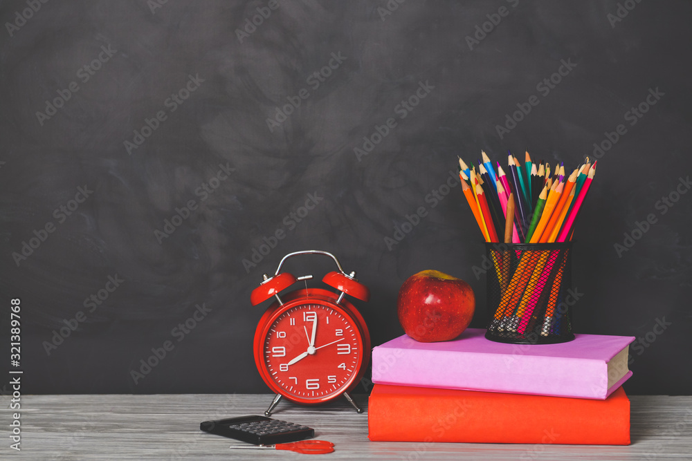 Set of school supplies, apple and clock on table near blackboard