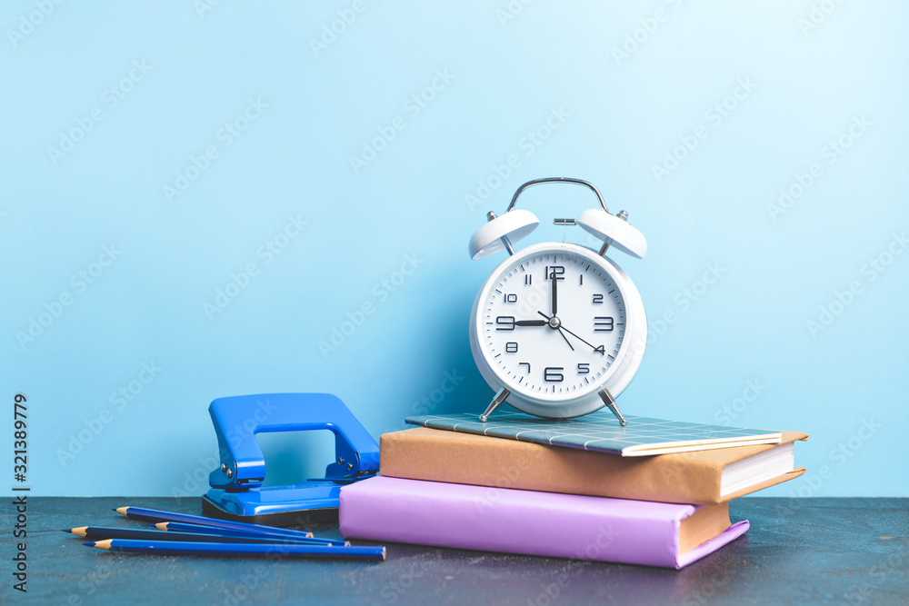 Set of school supplies and clock on table against color background