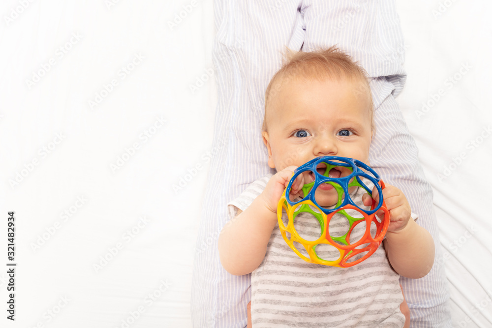 Little cute baby toddler play with colorful plastic ball laying on the back and hold toy near mouth