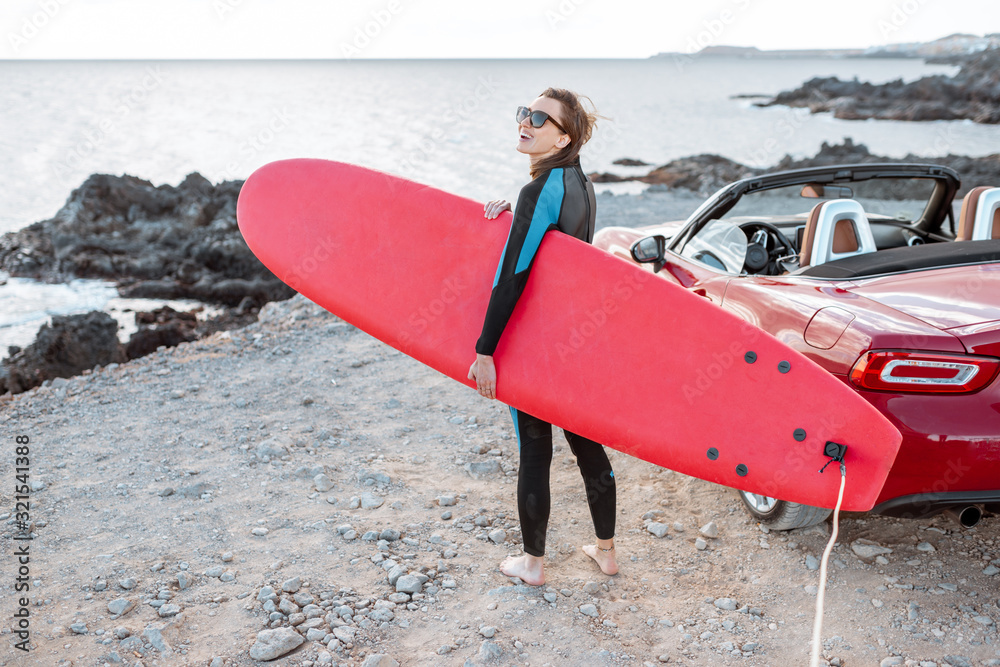 Portrait of a young woman surfer in swimsuit standing with surfboard on the rocky coast, enjoying be