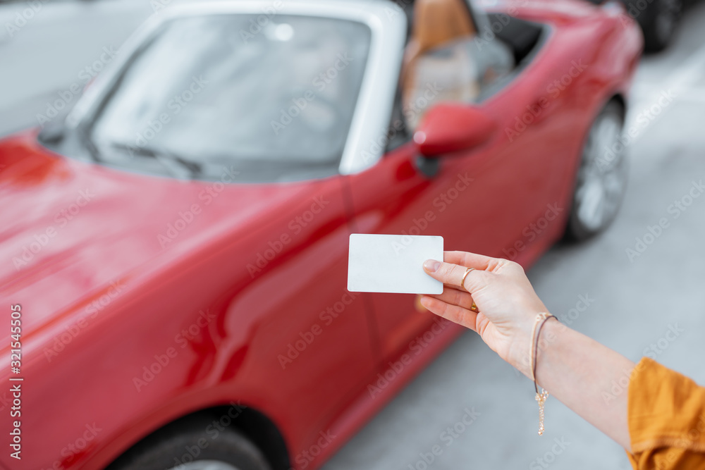 Woman holding plastic card with empty space to copy paste with red car on the background. Vehicle id