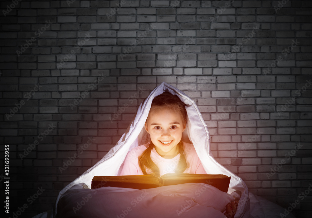 Happy little girl reading book in bed