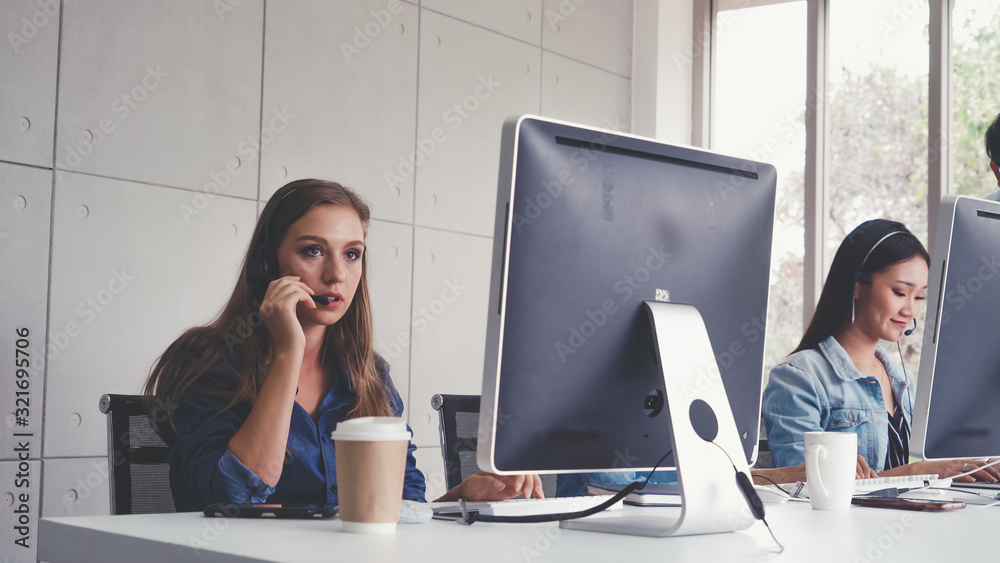 Customer support agent or call center with headset works on desktop computer while supporting the cu