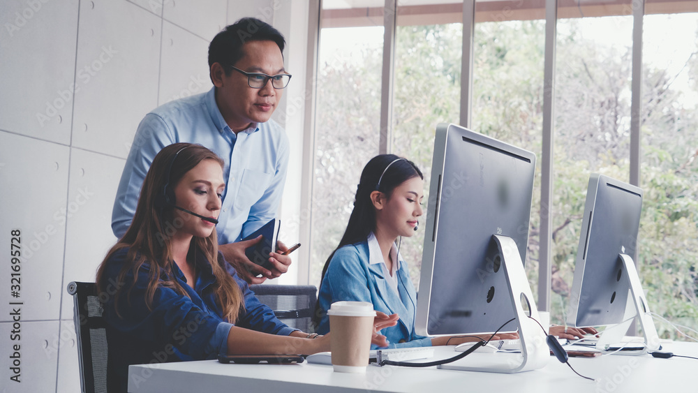 Customer support agent or call center with headset works on desktop computer while supporting the cu