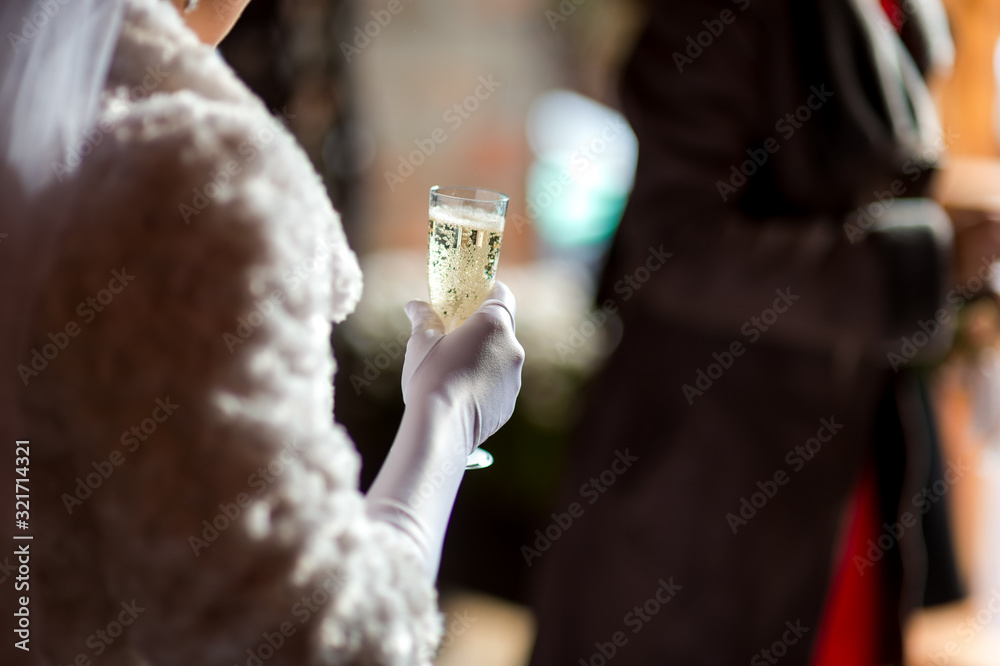 Stylish bride holds glass with champagne in hands. Blurred background. Selective focus. Wedding day.