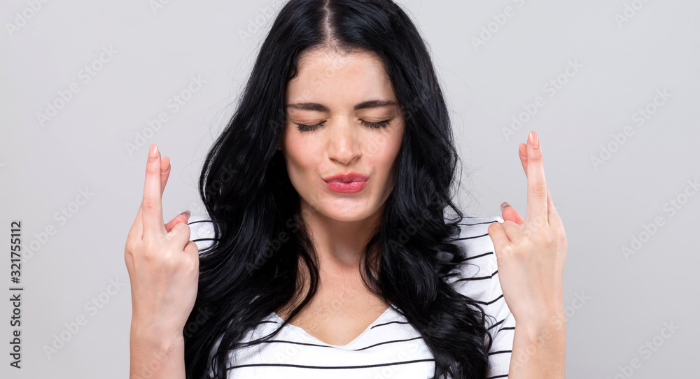 Young woman crossing her fingers and wishing for good luck on a gray background