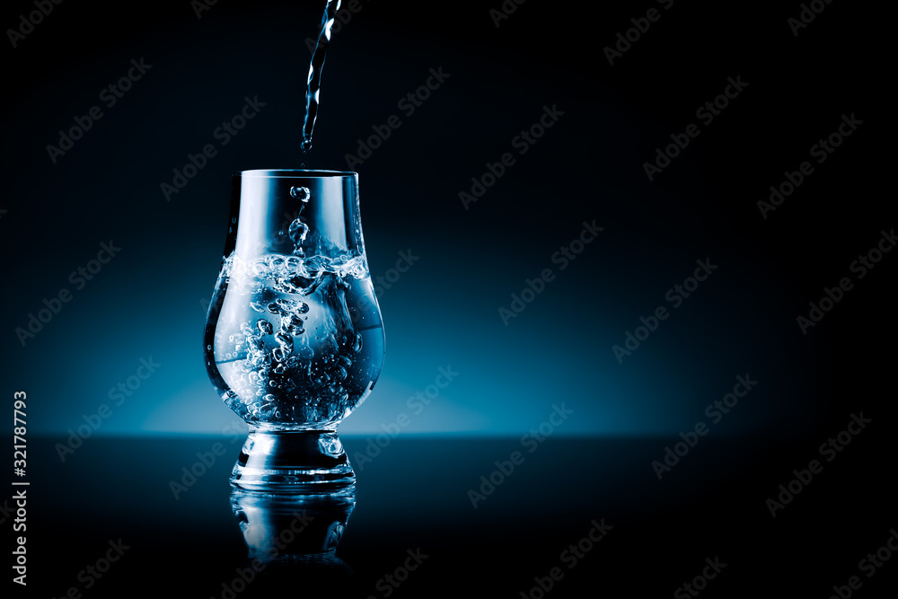 Liquid splashing into a glass - blue toned isolated on black with free text area