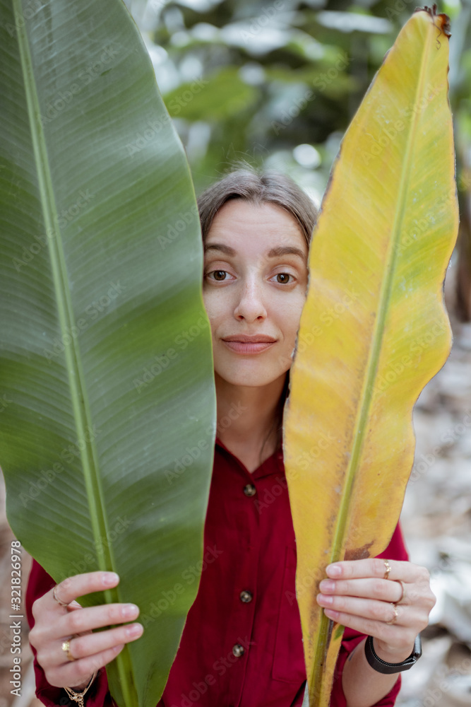 Portrait of a young woman hiding behind fresh and dry banana leaves on the plantation. Skin care con