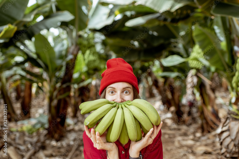 Portrait of a cute woman holding a stem with fresh green bananas in front of her face. Healthy eatin