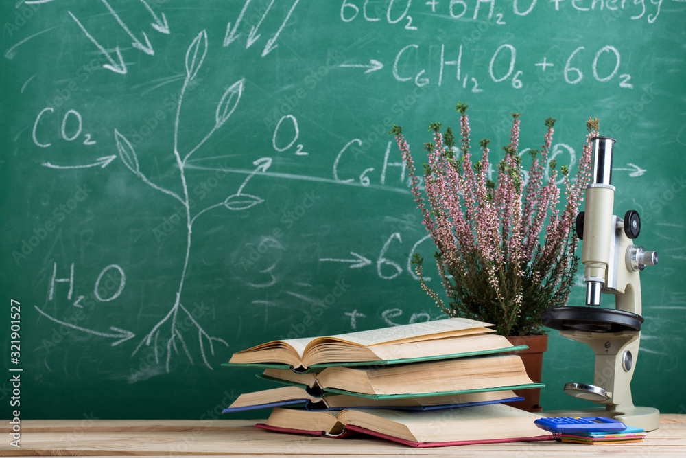 Education and sciences concept - book and microscope on the desk in the auditorium, photosynthesis f