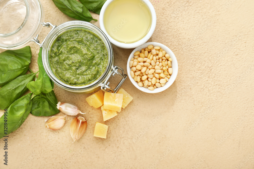 Bowl with pesto sauce and ingredients on color background