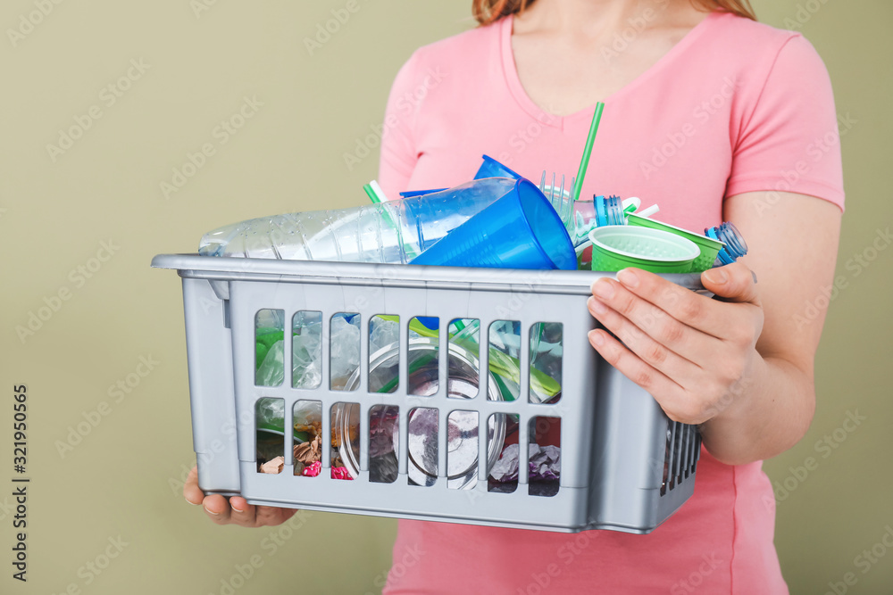 Woman holding basket with garbage on color background, closeup