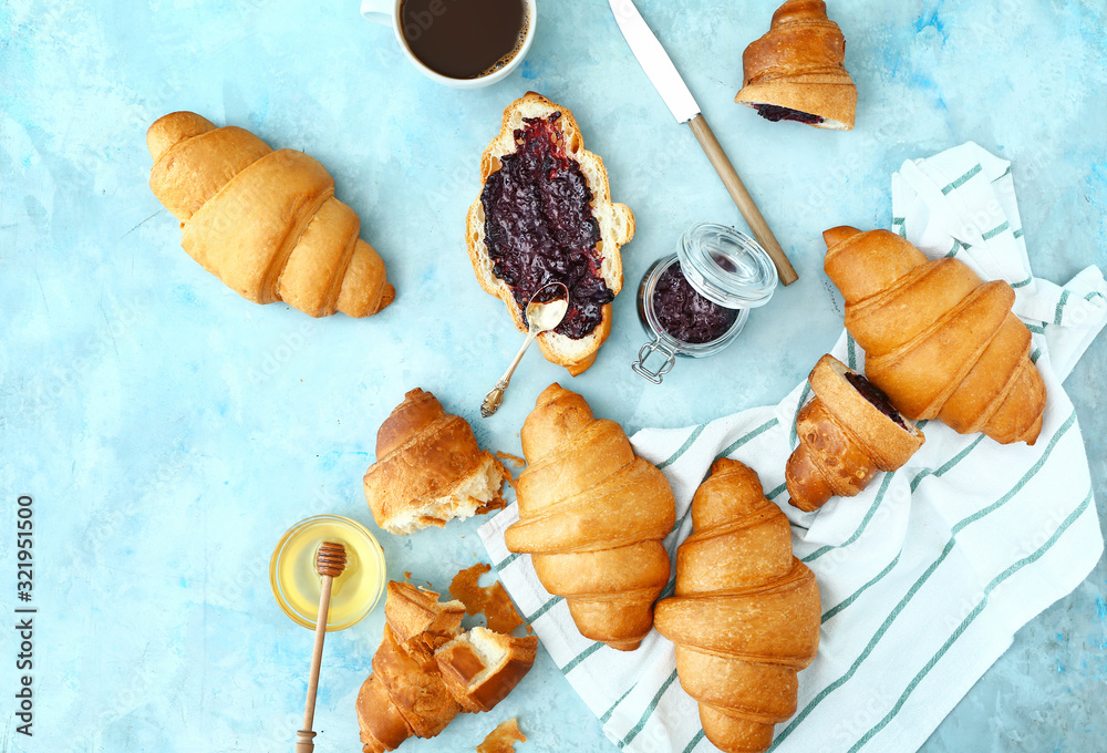 Tasty sweet croissants with jam, honey and coffee on color background