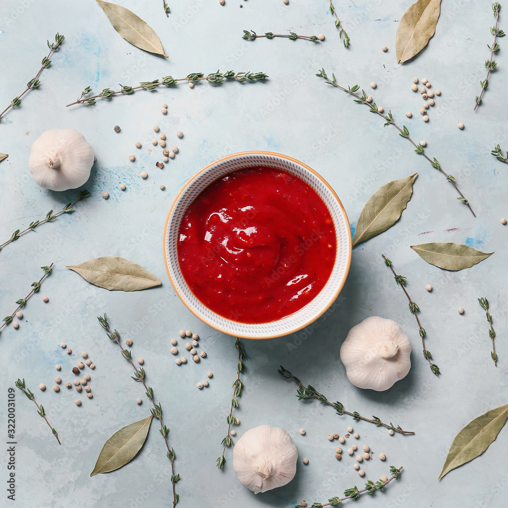 Bowl with tomato sauce and spices on color background