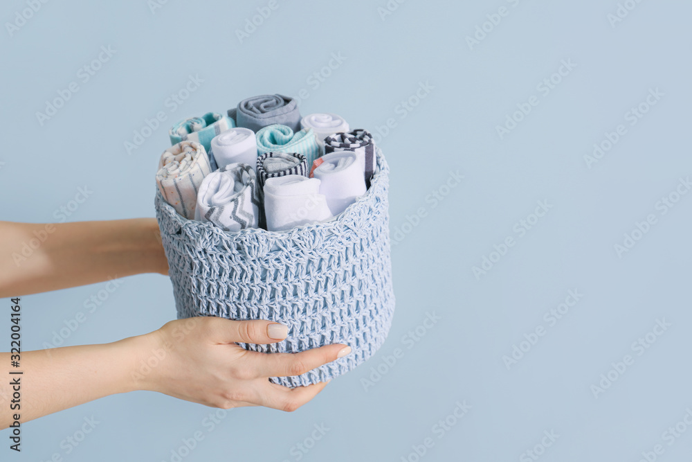 Female hands holding basket with socks on color background