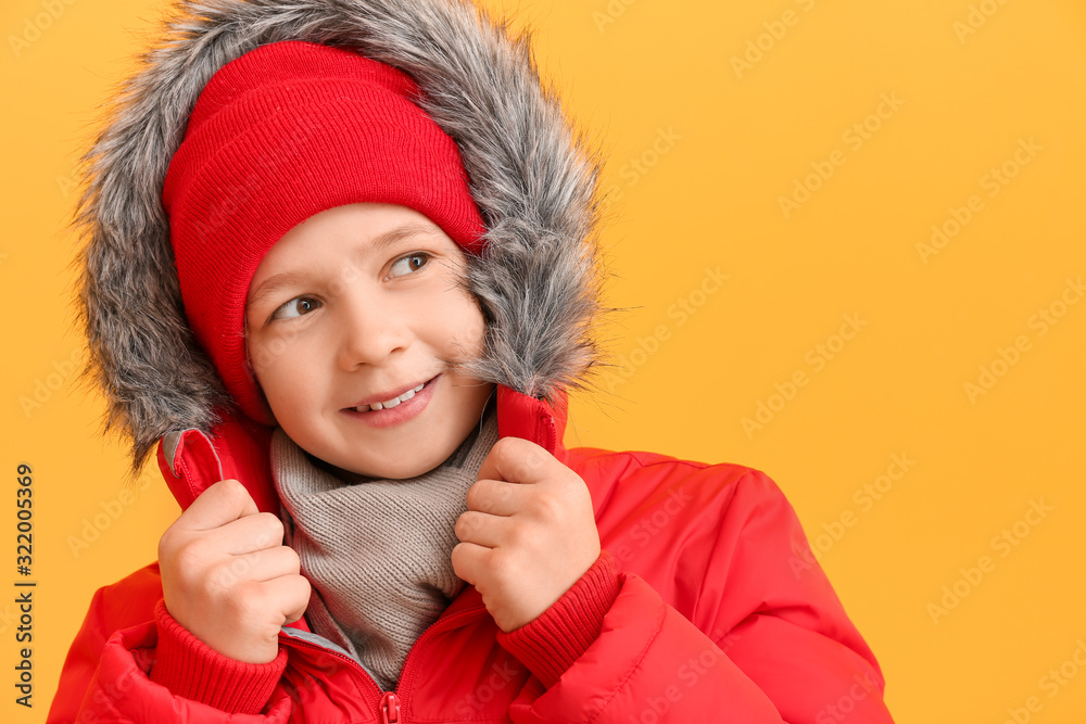 Cute little boy in winter clothes on color background