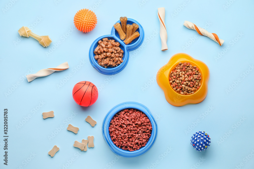 Bowls with pet food and toys on color background