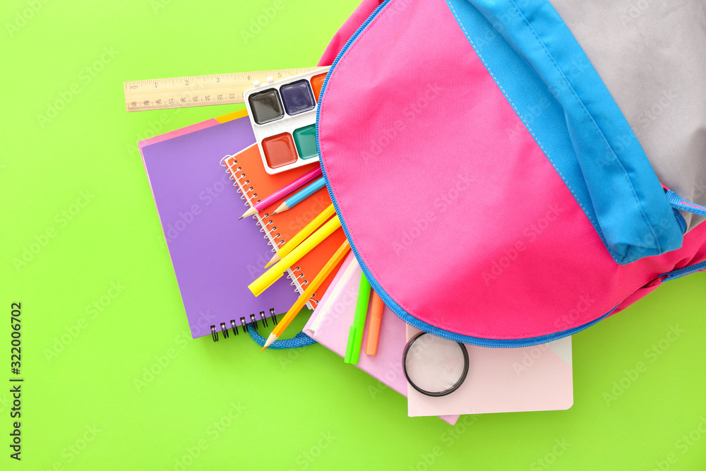 School backpack with stationery on color background