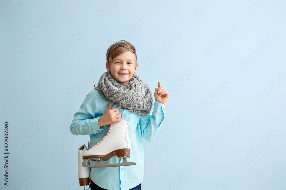 Cute little boy with ice skates against color background