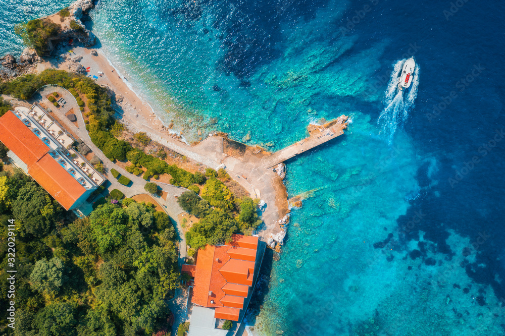 Aerial view of sea coast with clear blue water, boats, pier, hotels and green trees in summer at sun