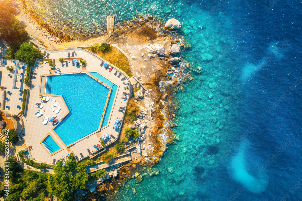 Aerial view of pool, sandy beach, stones, green trees, people and sea with transparent blue water at