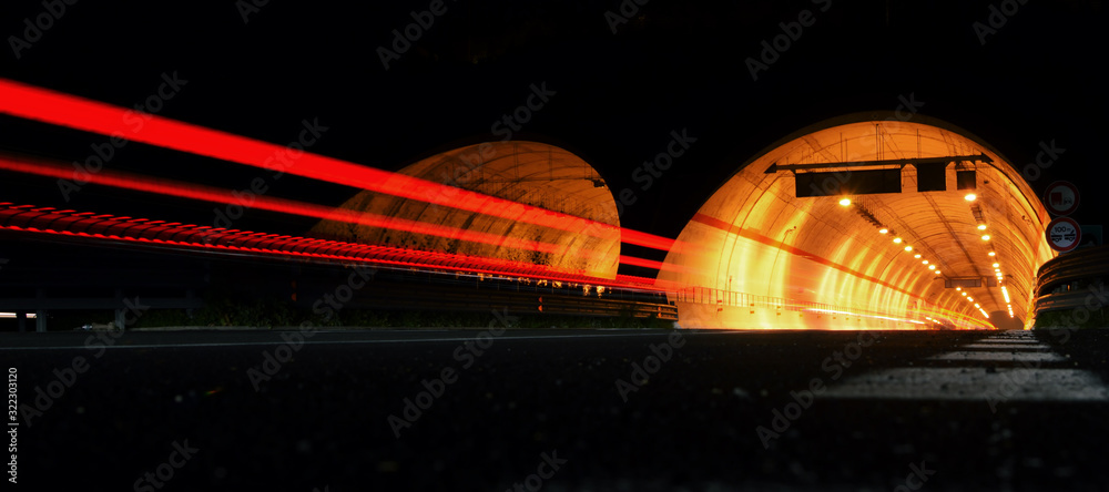 Street at night with red trails of cars in front of a tunnel