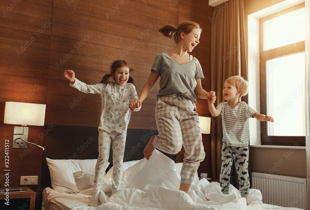 happy family mother and children son and daughter jumping, laughing, playing in bed.