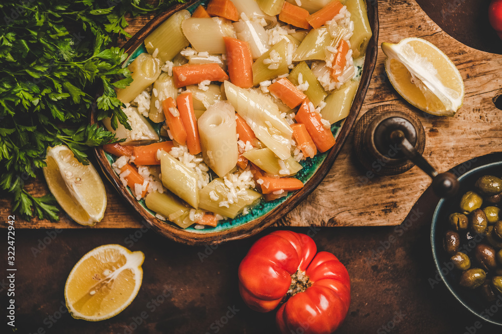 Flat-lay of Turkish traditional leek, rice and carrot meze dish woth lemon on wooden board over rust