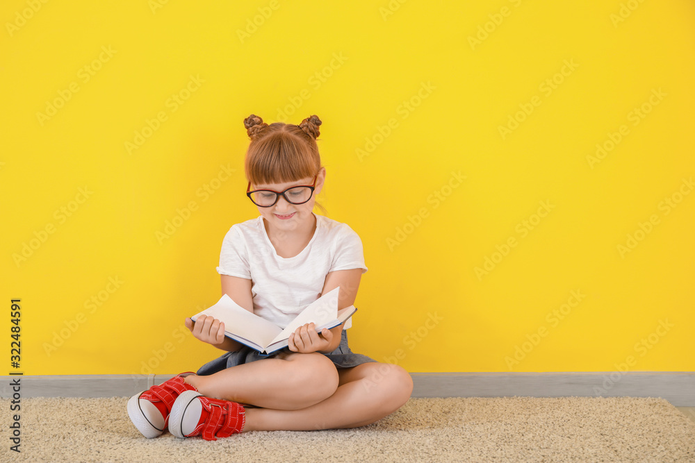 Cute little girl with book sitting near color wall