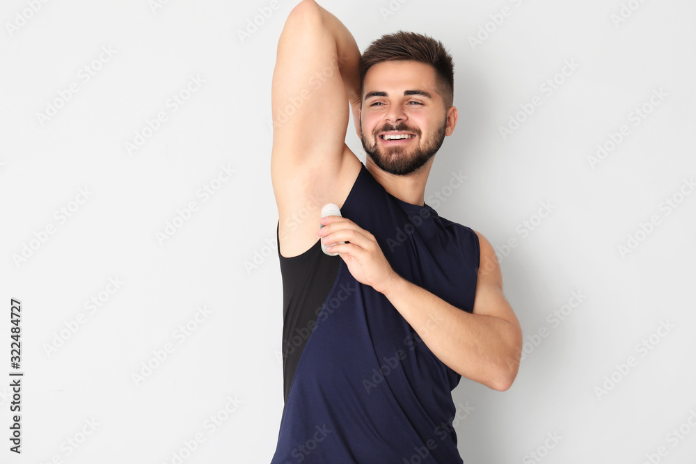 Handsome young man using deodorant on light background