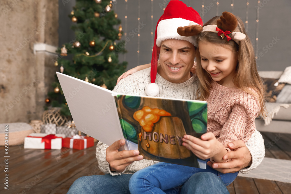 Little daughter with father reading book on Christmas eve at home