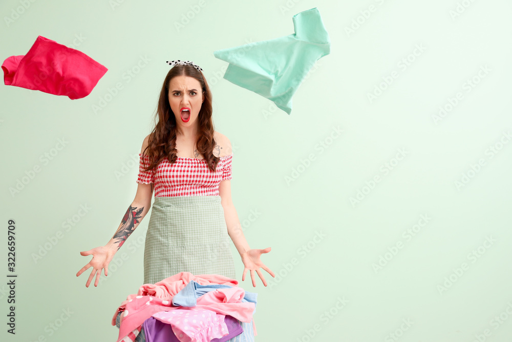 Angry housewife with laundry on color background