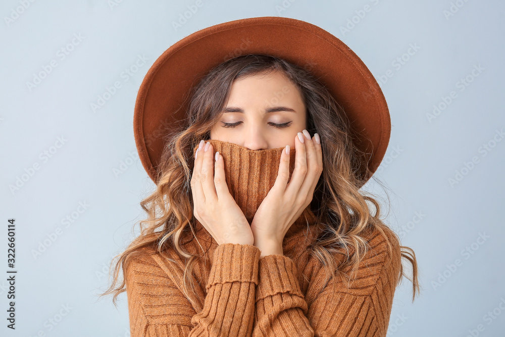 Beautiful young woman in warm sweater on light background