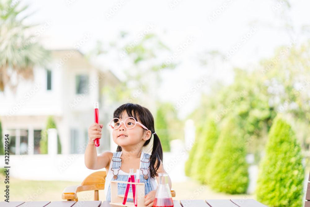 小科学家亚洲蹒跚学步的书呆子女孩戴着眼镜，把红色液体放进烧瓶里摇晃。主页