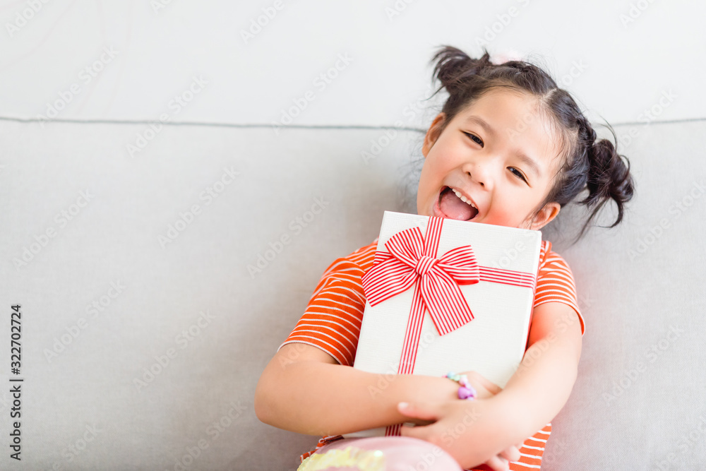 Little asian girl smile and excited and holding red gift box on sofa in living room background.child